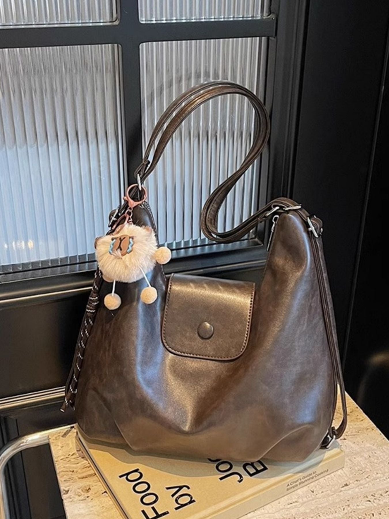 Slouchy coffee brown pu leather shoulder bag with braided strap detail and fluffy charm.