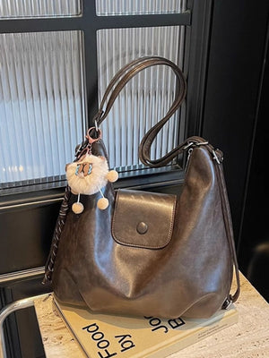 Slouchy coffee brown pu leather shoulder bag with braided strap detail and fluffy charm.