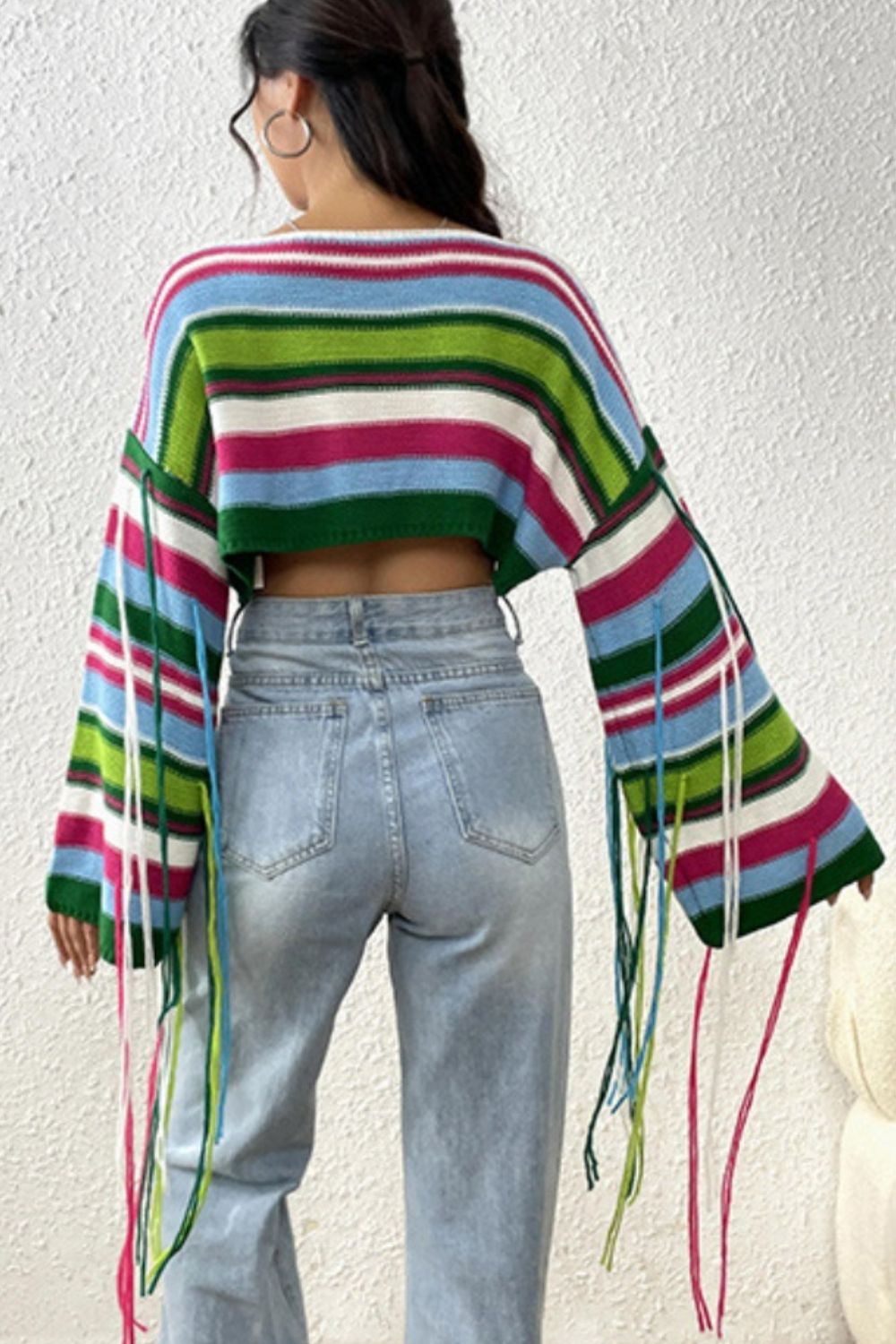Cropped knit sweater with colorful stripes and fringe detail on sleeves.