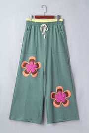 Green cotton sweatpants with wide legs, drawstring, and floral appliques.