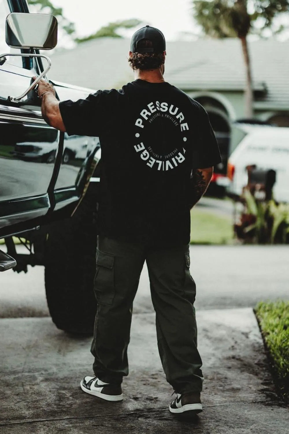 Black graphic tee with circular "Pressure Privilege" print, crew neck, short sleeves.