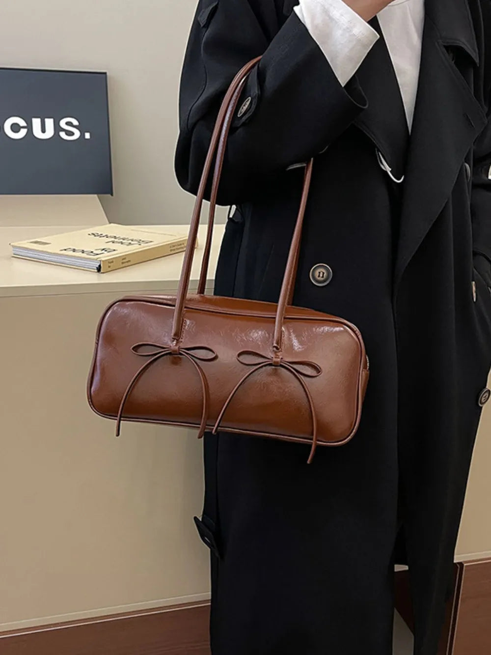 Brown patent leather shoulder bag with bow details and thin straps.