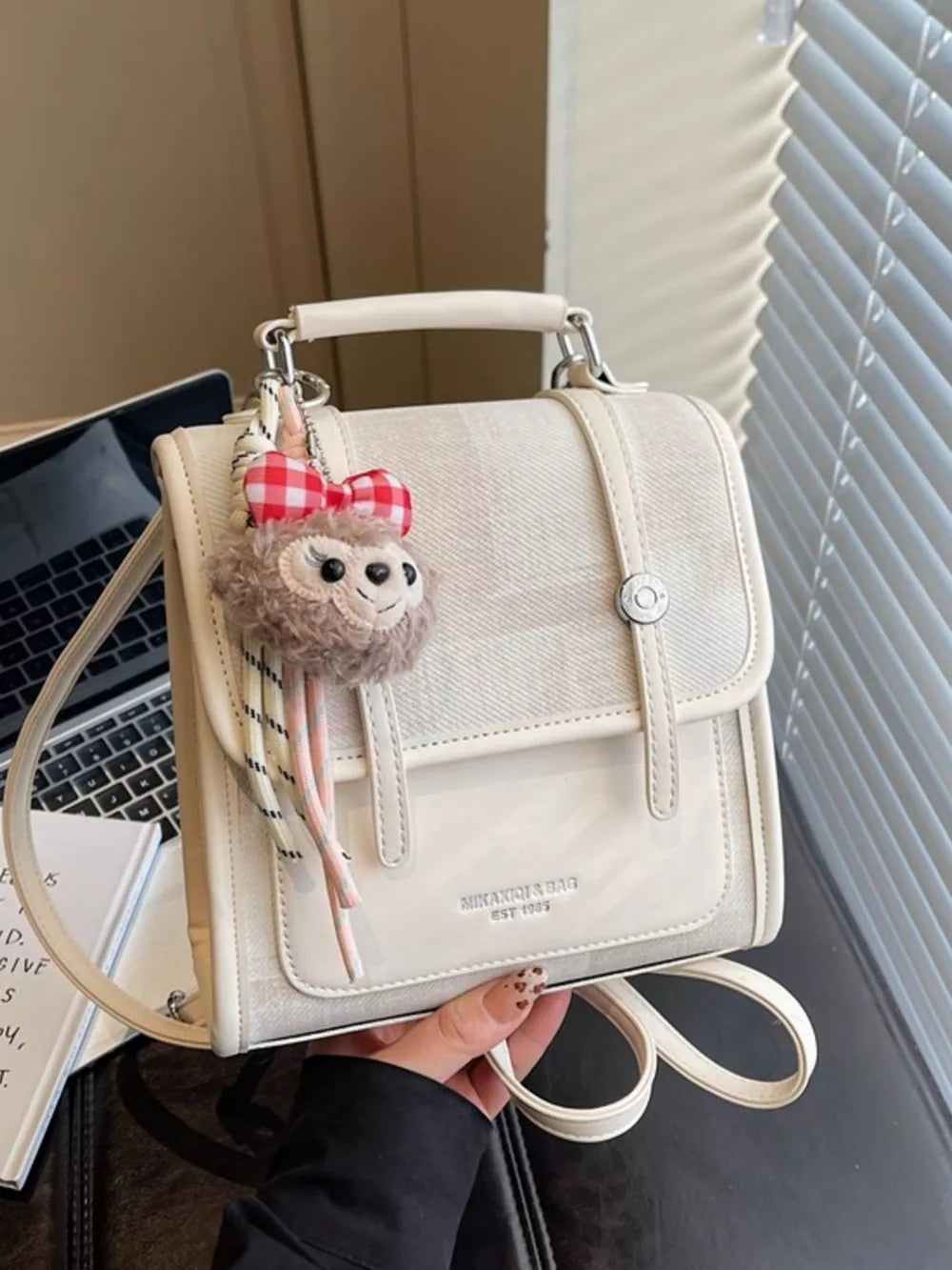 Chic mini flap backpack in white with plush sloth charm and adjustable straps.