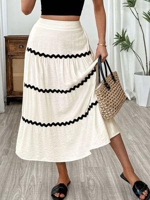 Elegant tiered midi skirt in beige with black wavy trim, flowing A-line cut.