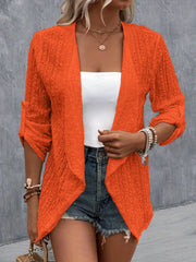 Orange open-weave cardigan with draped front and rolled sleeves, styled with denim shorts.