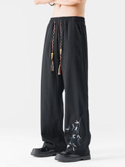Black wide-leg men's sweatpants with embroidered bamboo detail and braided drawstring.