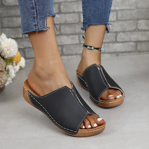 Black vegan leather asymmetrical slides with white stitching detail.