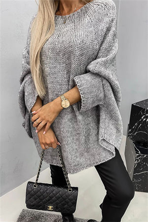 Gray knit sweater with cape sleeves and a relaxed fit, styled with black pants and a quilted handbag.