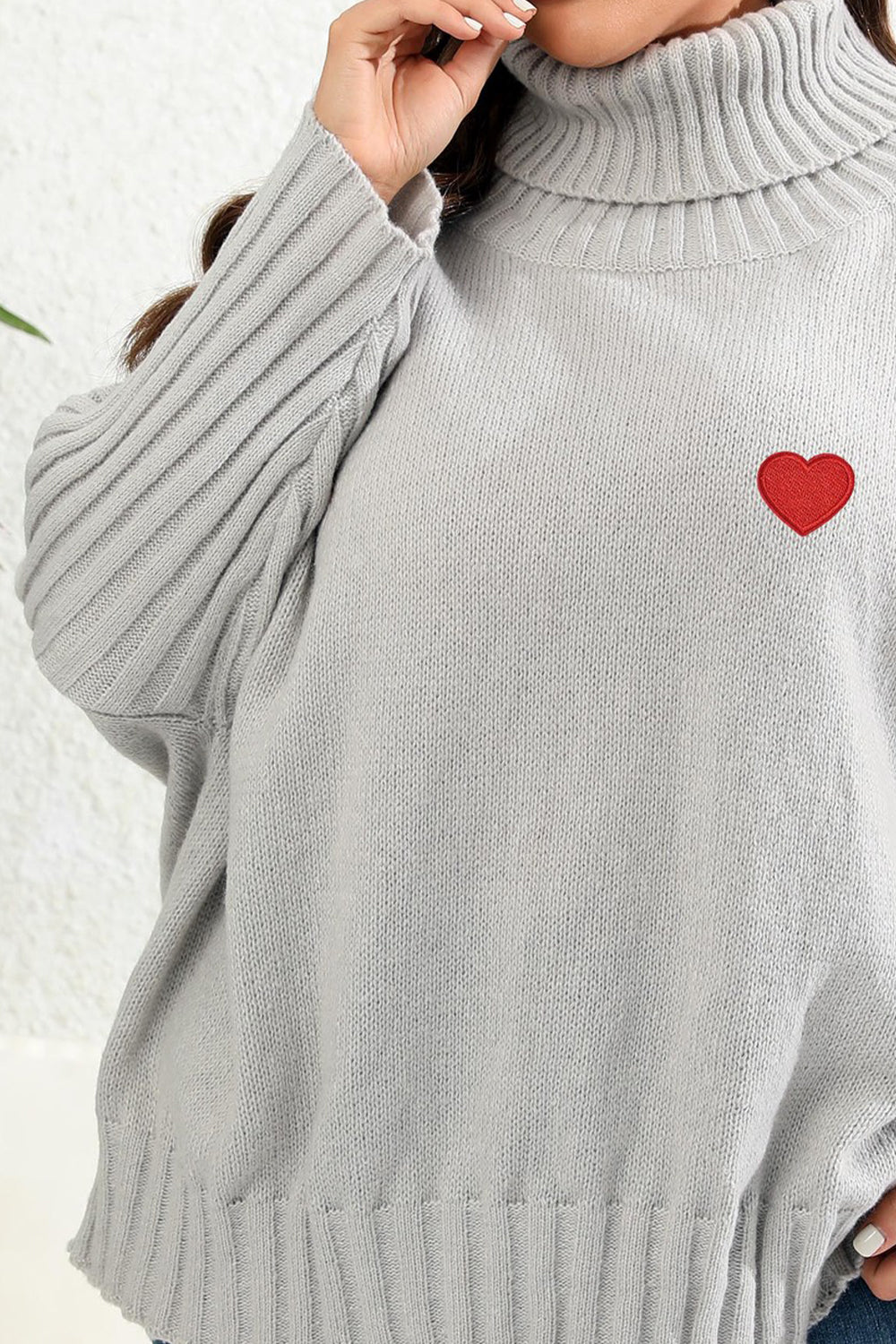 Light gray turtleneck sweater with batwing sleeves and a red heart appliqué.