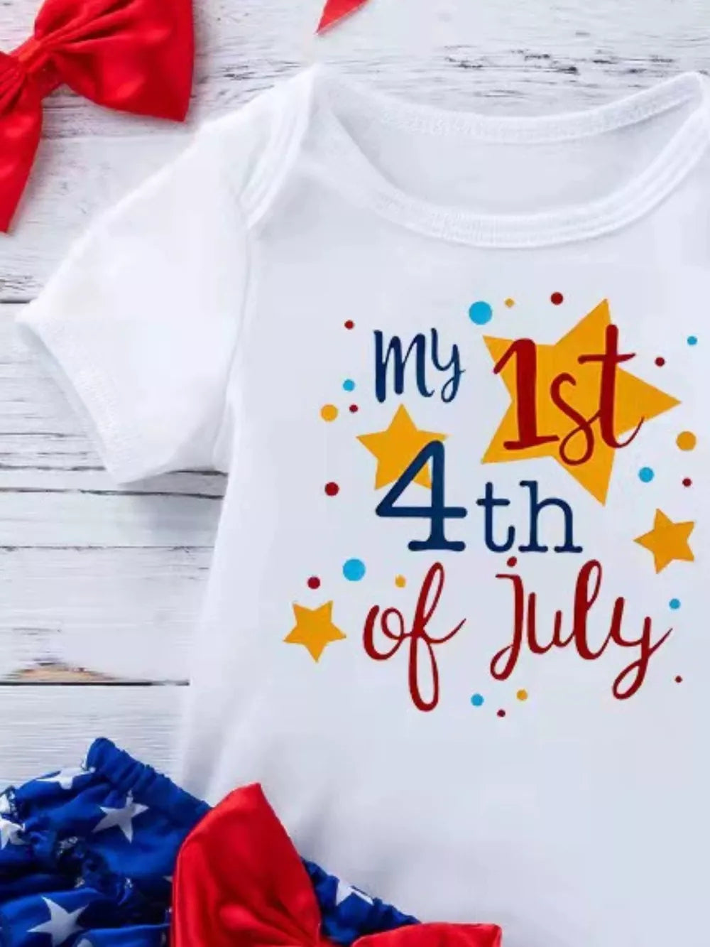 White baby onesie with "my 1st 4th of July" text and stars, paired with patriotic bloomer shorts and bow.