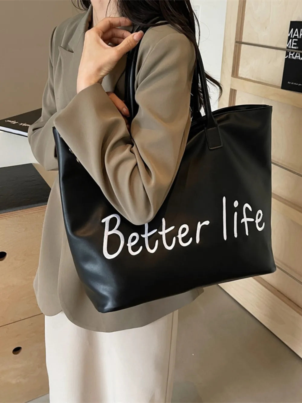 Black tote bag with white Better Life graphic, held by a person wearing a blazer.