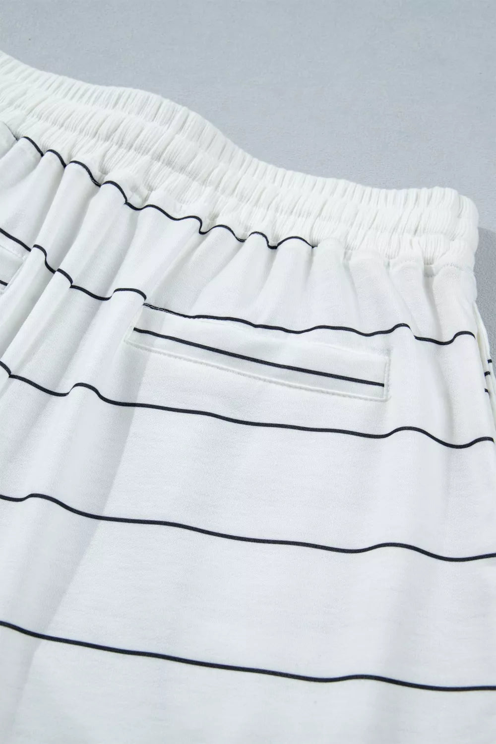 White polyester bikini shorts with black stripes and drawstring waist.