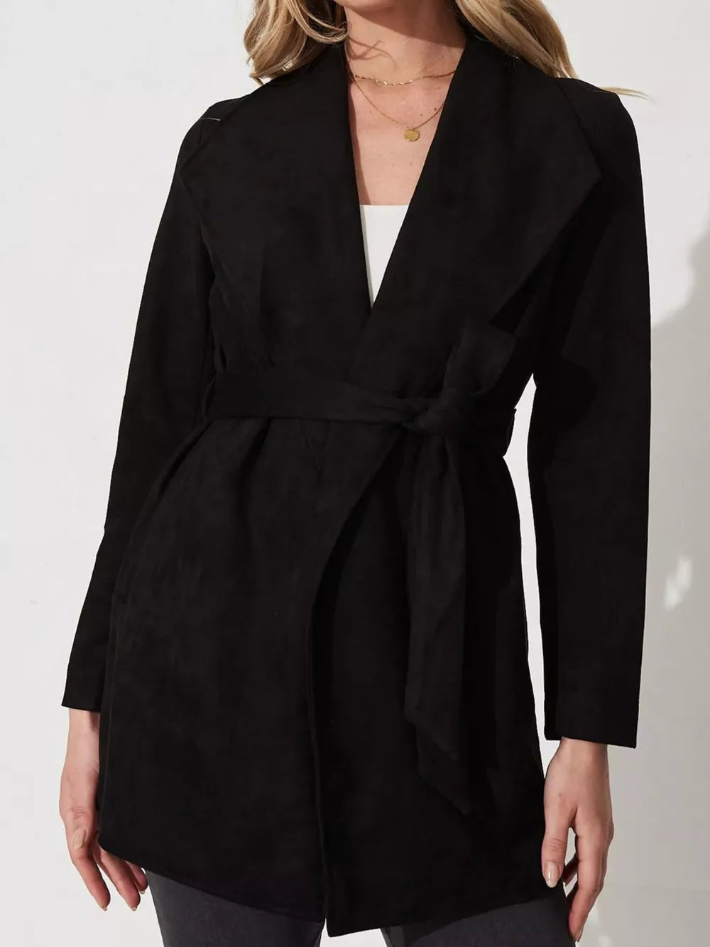Black suede duster coat with tie waist and open collar, worn by a woman.