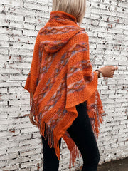 Textured knit hooded cape in terracotta with fringe and colorful stripes.