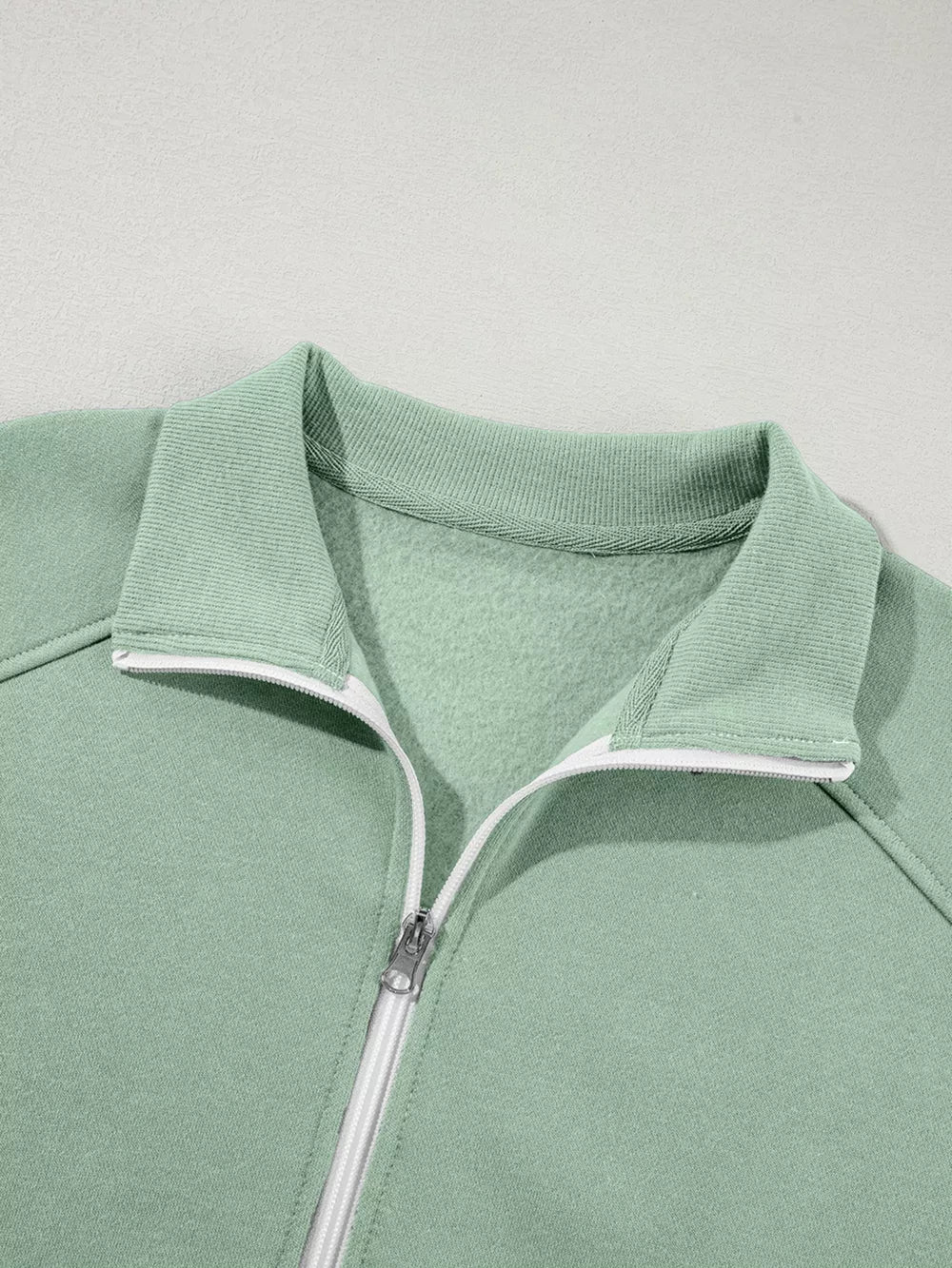 Sage zip-up jacket with collar and white zipper detail, made of cotton.