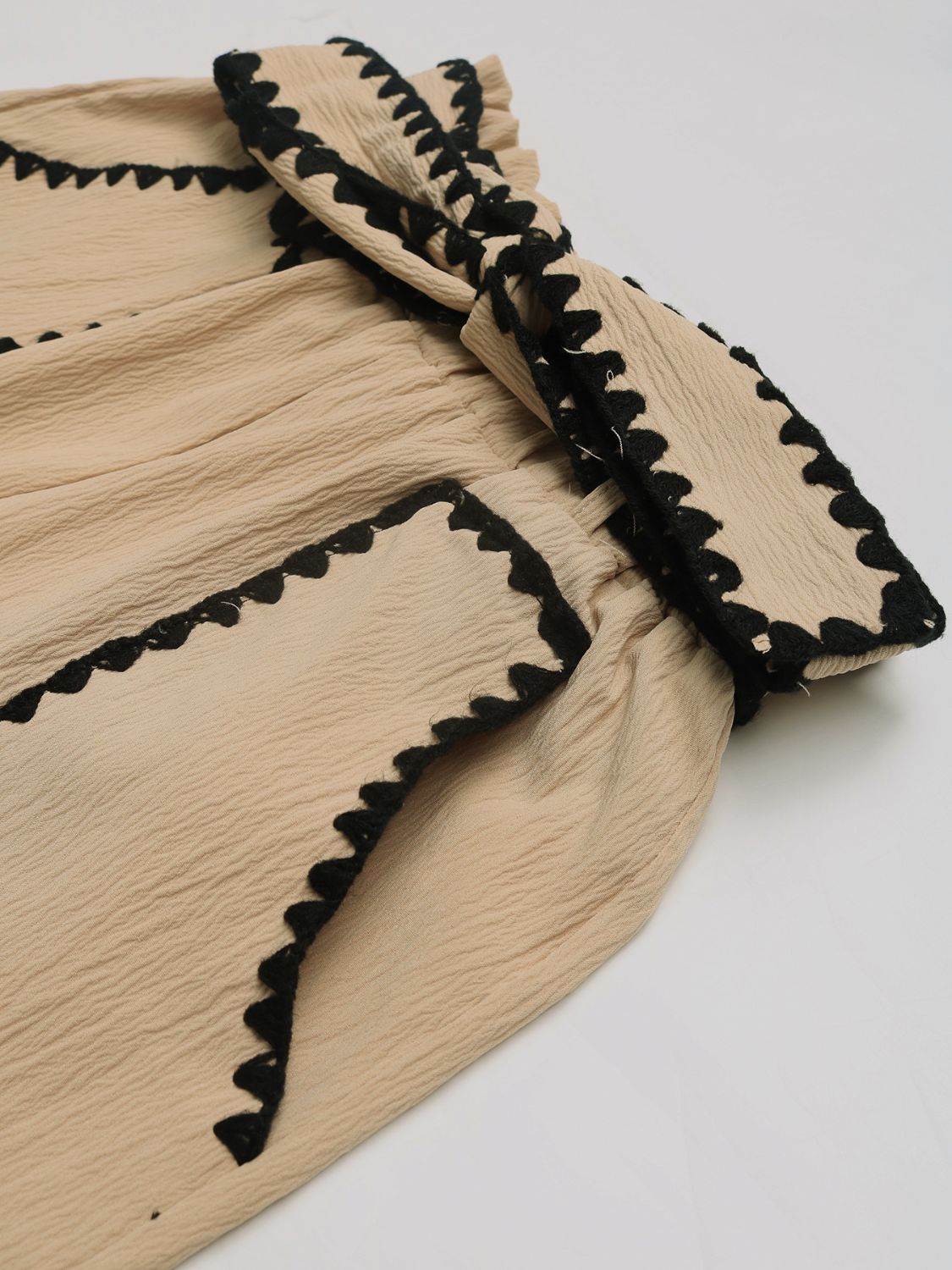 Tan paperbag shorts with black scalloped trim detail and textured fabric.