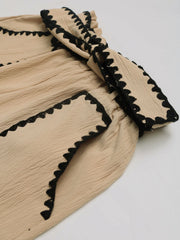 Tan paperbag shorts with black scalloped trim detail and textured fabric.