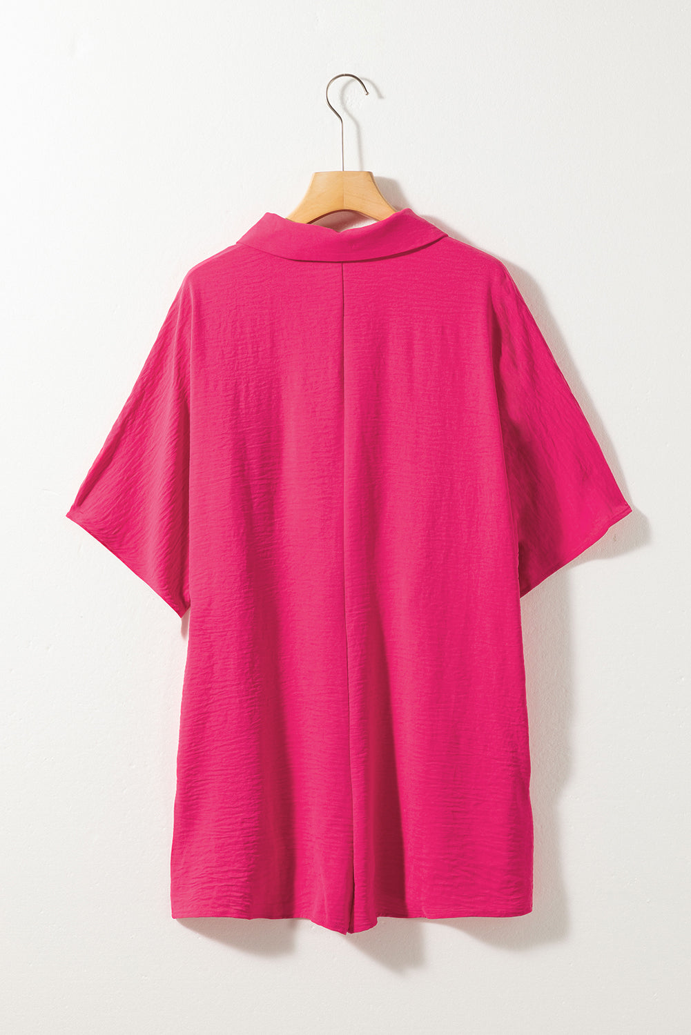 Oversized shirt romper in hot pink with textured fabric and short sleeves.
