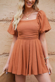 Ochre square neck puff sleeve romper with cinched waist and pleated skirt.