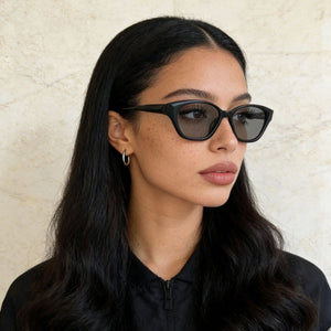 Black acetate cat-eye sunglasses with dark lenses, worn by a woman.
