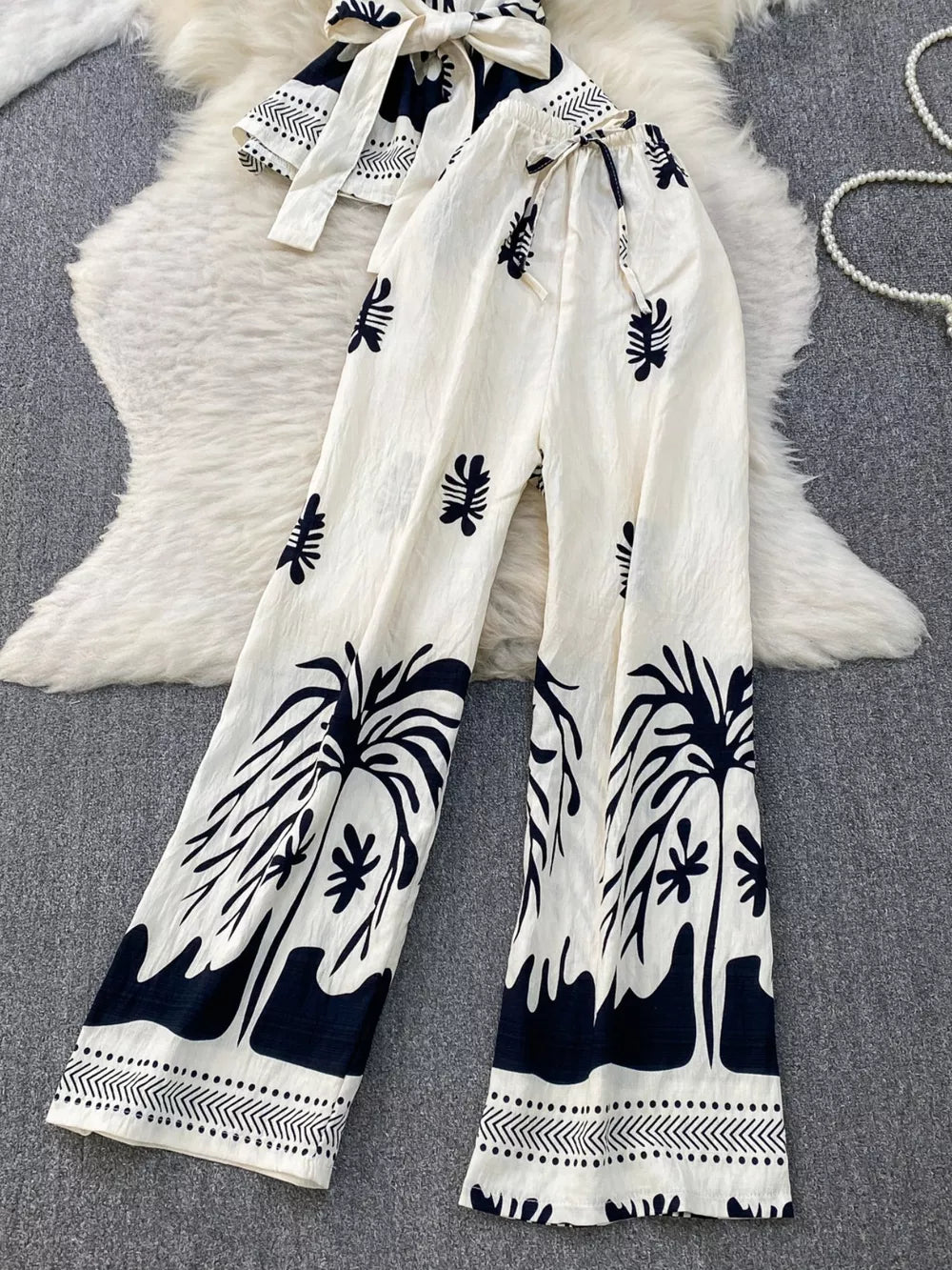 Tropical print two-piece set with belted detail, featuring wide-leg pants and a tie-front top in white with black palm tree
