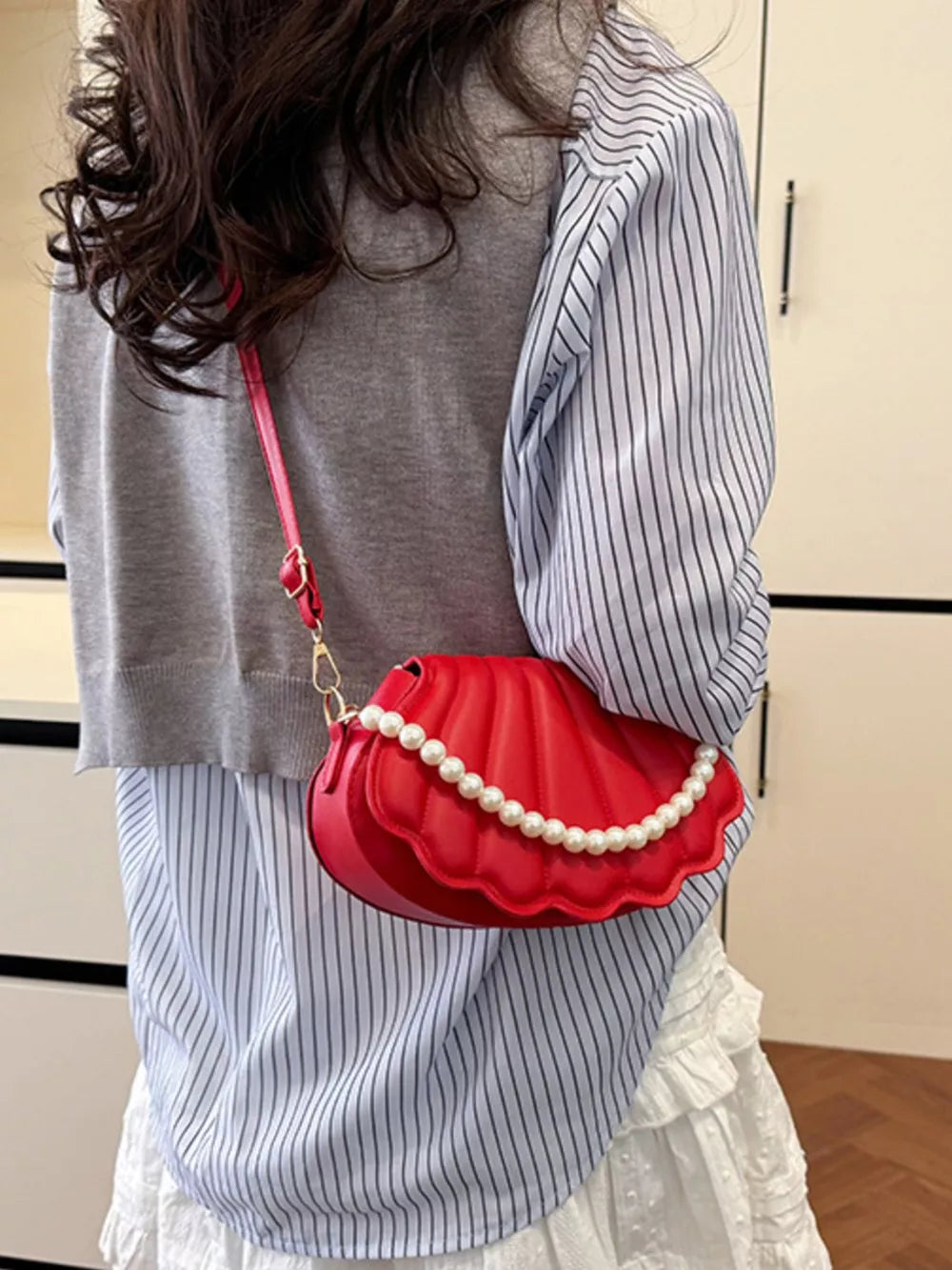 Red shell crossbody bag with pearl trim and a gold chain strap.