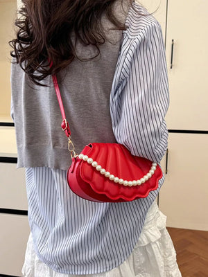 Red shell crossbody bag with pearl trim and a gold chain strap.