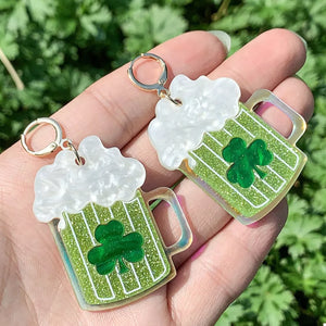 Gold dangle earrings with green beer mug charms featuring shamrocks and white foamy tops.