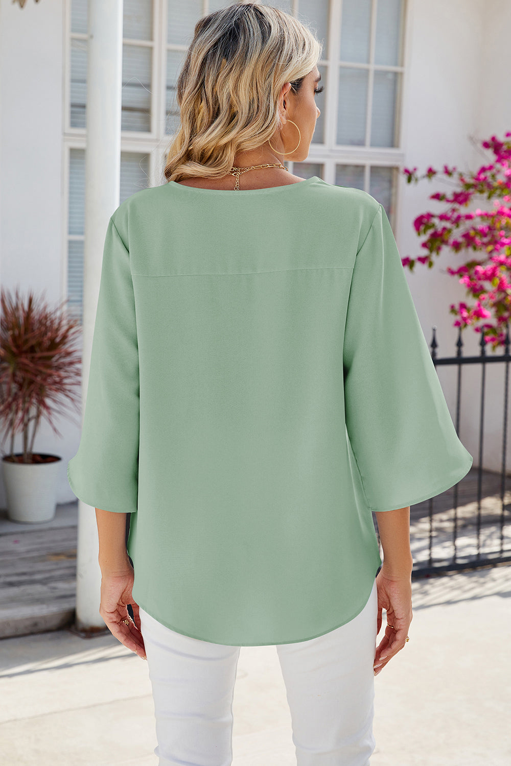 Light green flowy blouse with asymmetric bell sleeves and a curved hem.