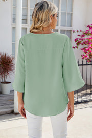 Light green flowy blouse with asymmetric bell sleeves and a curved hem.