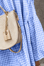 Blue gingham maxi dress with smocked bodice and flutter sleeves, shown with a straw bag.