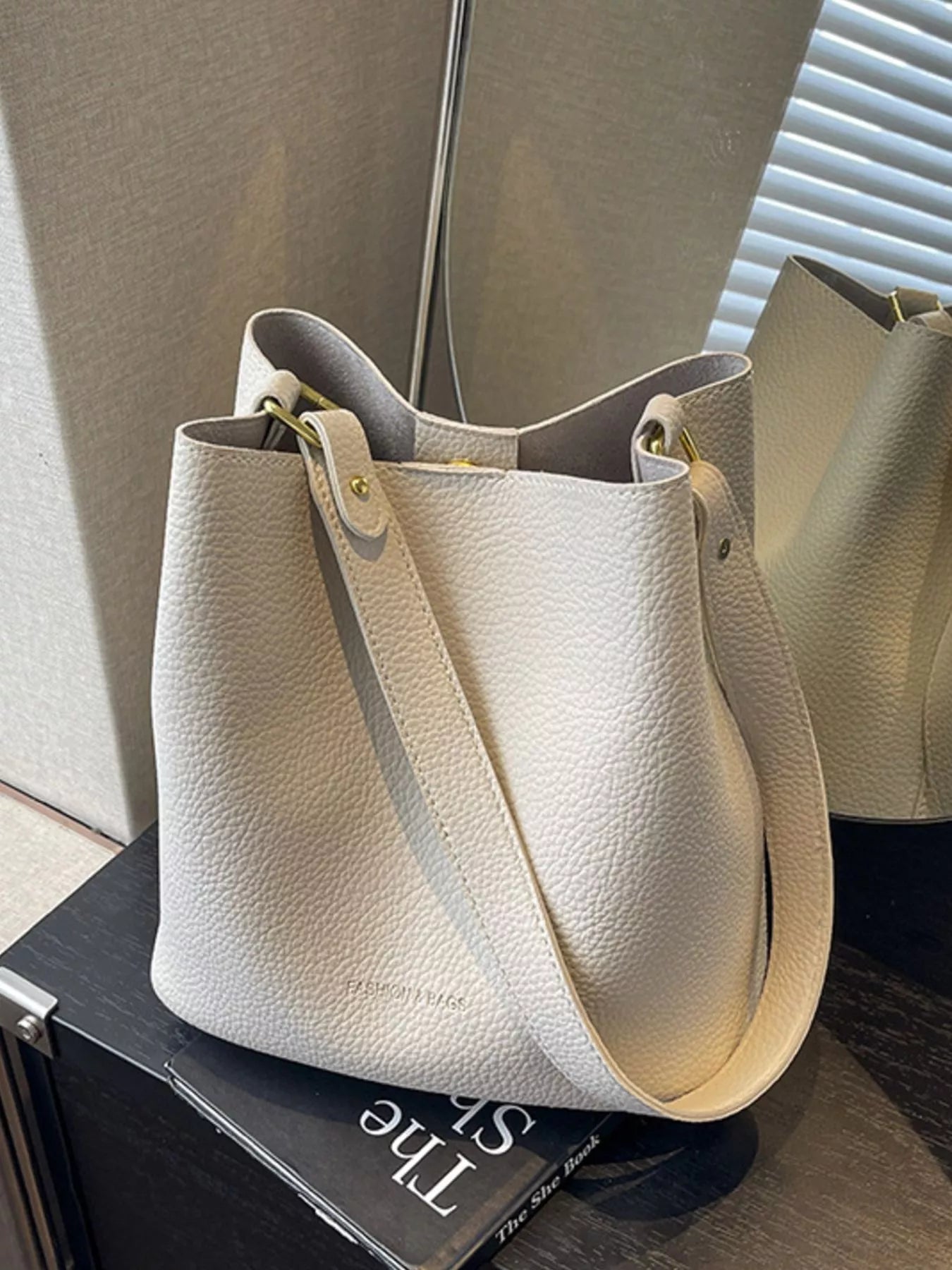 Off-white pebbled leather tote bag with adjustable strap and gold hardware.
