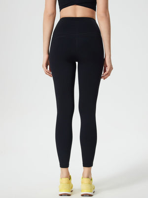 Black high-waisted leggings with contouring detail and pocket, worn with yellow sneakers.