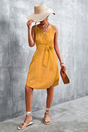 Mustard daisy print slip dress with tie waist and V-neck, styled with a straw hat and sandals.
