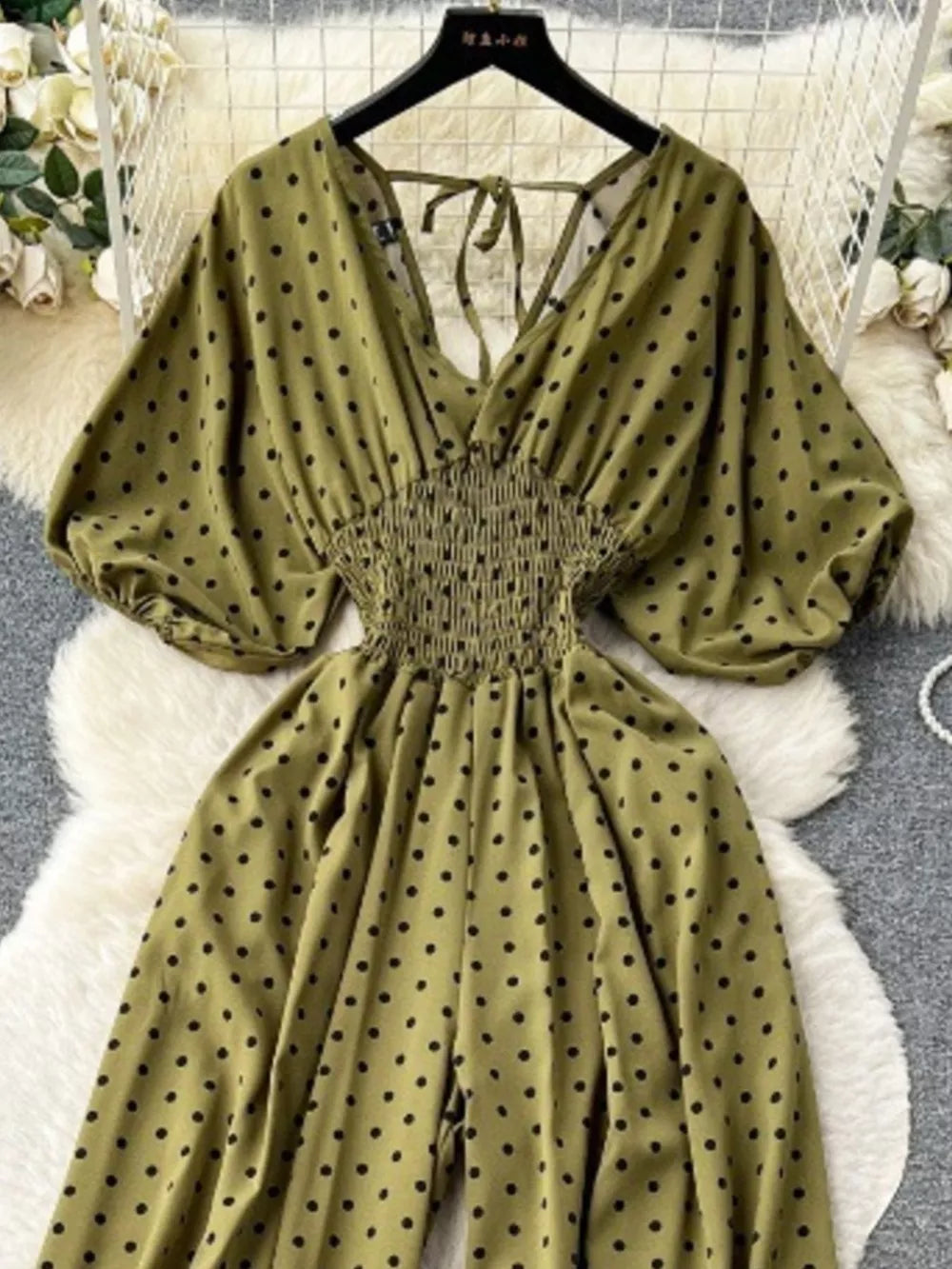 Army green polka dot smocked wide-leg romper with tie-back V-neck and puff sleeves.