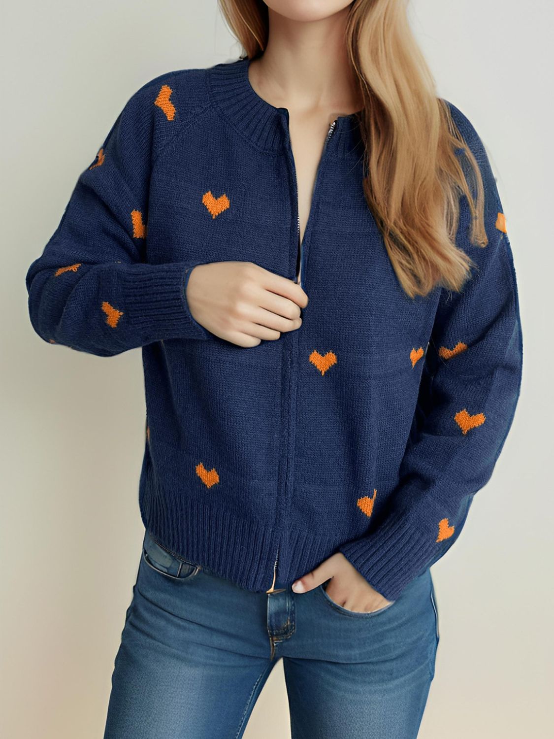 Dark blue zip-through knit cardigan with allover orange heart appliqué, crew neck, and ribbed cuffs.