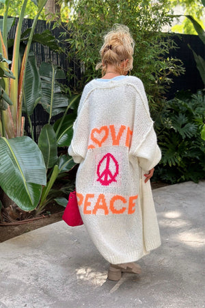White knit maxi cardigan with orange LOVE and PEACE text and pink peace sign graphic on back.