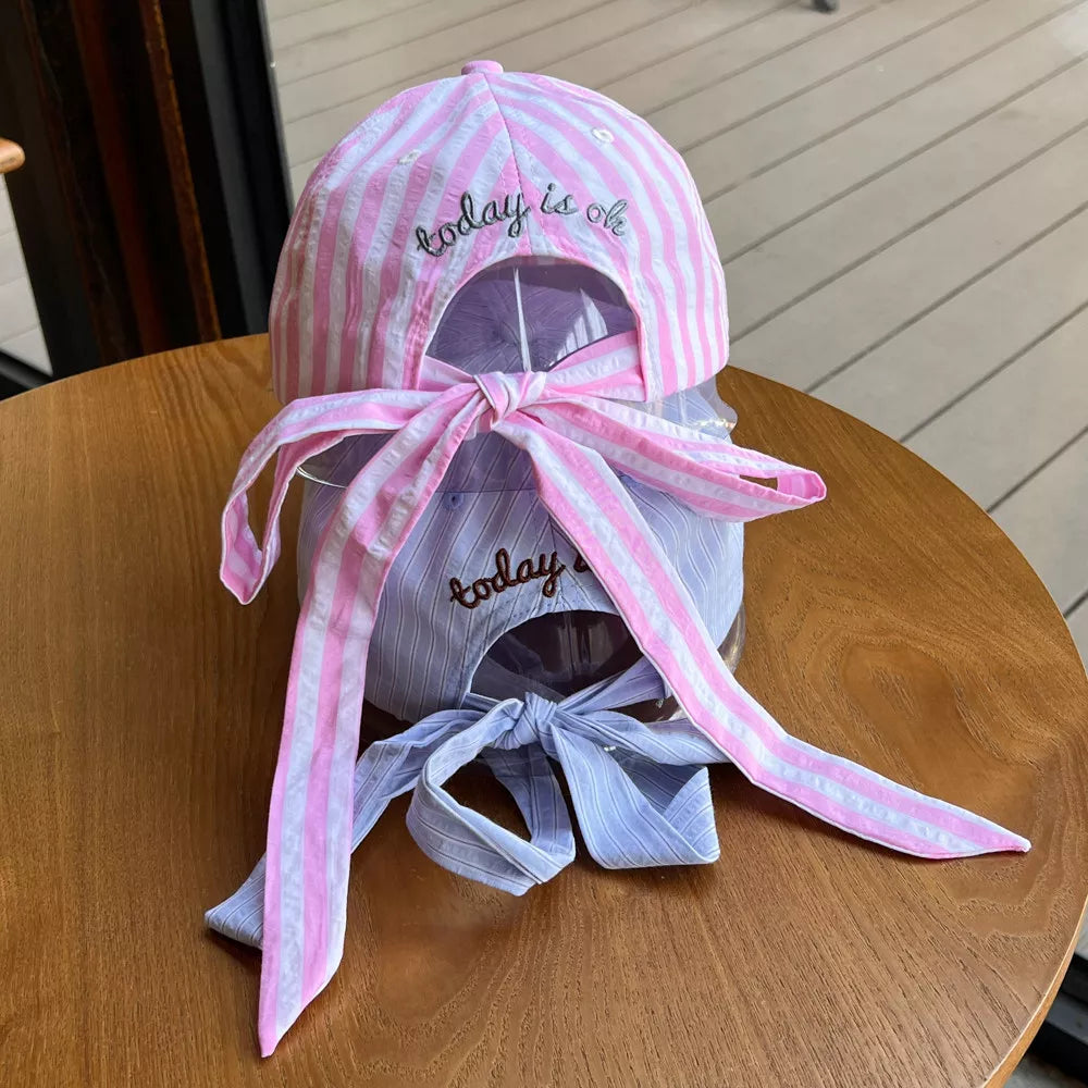 Pastel pink and white striped cotton baseball cap with embroidered text and bow detail.