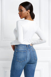 White long sleeve bodysuit with a scoop neck, styled with blue jeans.