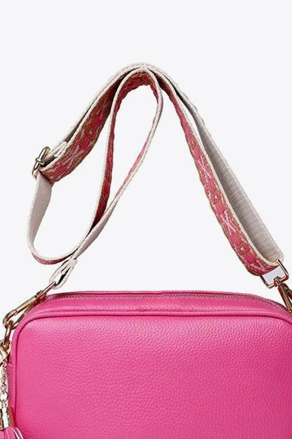 Textured crossbody bag in fuchsia pink with patterned strap and tassel detail.