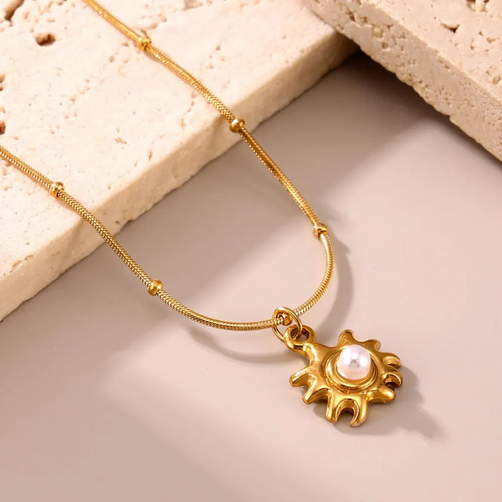 Gold sunburst pendant necklace with pearl detail and beaded chain.