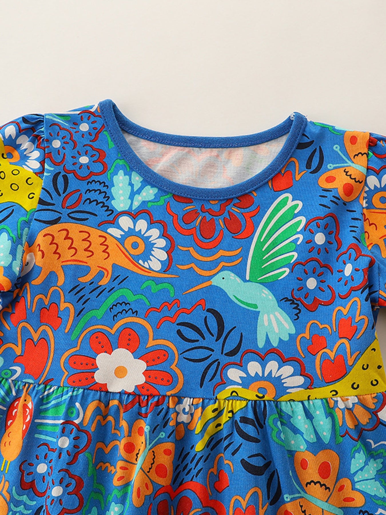 Blue cotton toddler dress with whimsical animal and floral print, ruffled sleeves, and round neckline.