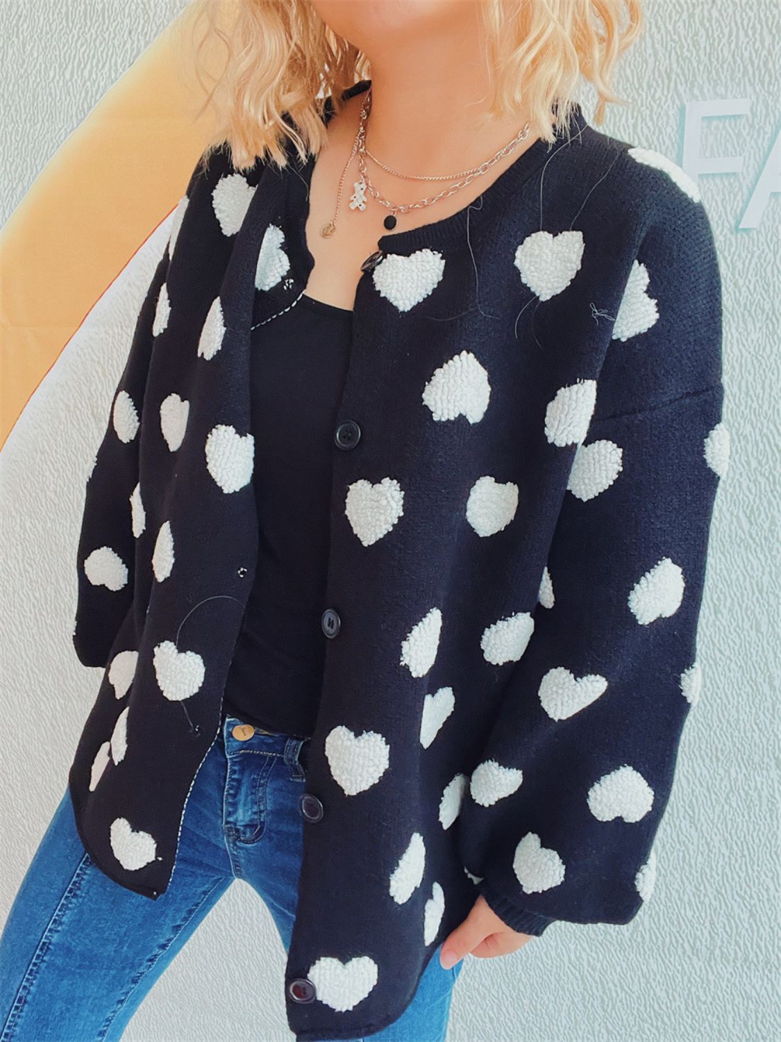 Black acrylic button-down cardigan with white textured heart motif, crew neck, and long sleeves.