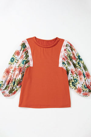 Orange-red blouse with floral patchwork balloon sleeves and a round neckline.