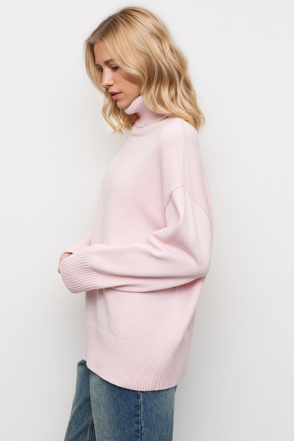 Oversized pink turtleneck sweater with ribbed cuffs and hem, styled with jeans.