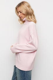 Oversized pink turtleneck sweater with ribbed cuffs and hem, styled with jeans.