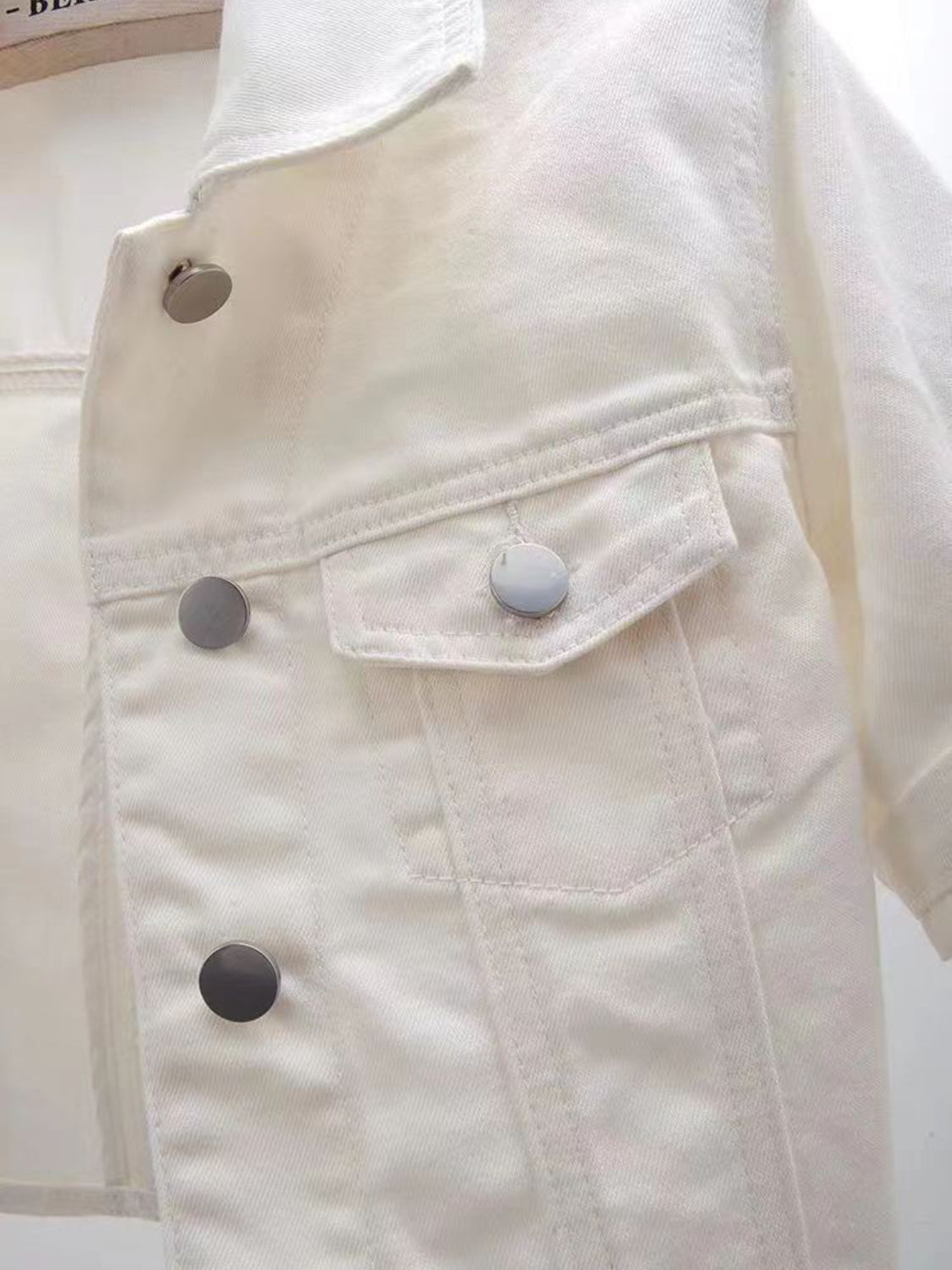 White denim trucker jacket with cropped sleeves and silver buttons.