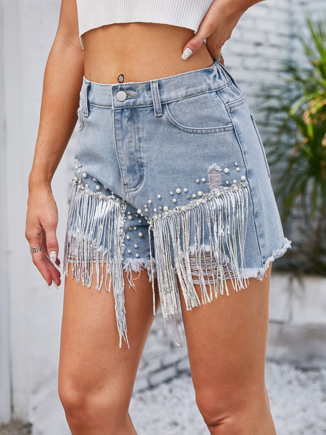 Light wash denim shorts with pearl embellishments and silver fringe detail.