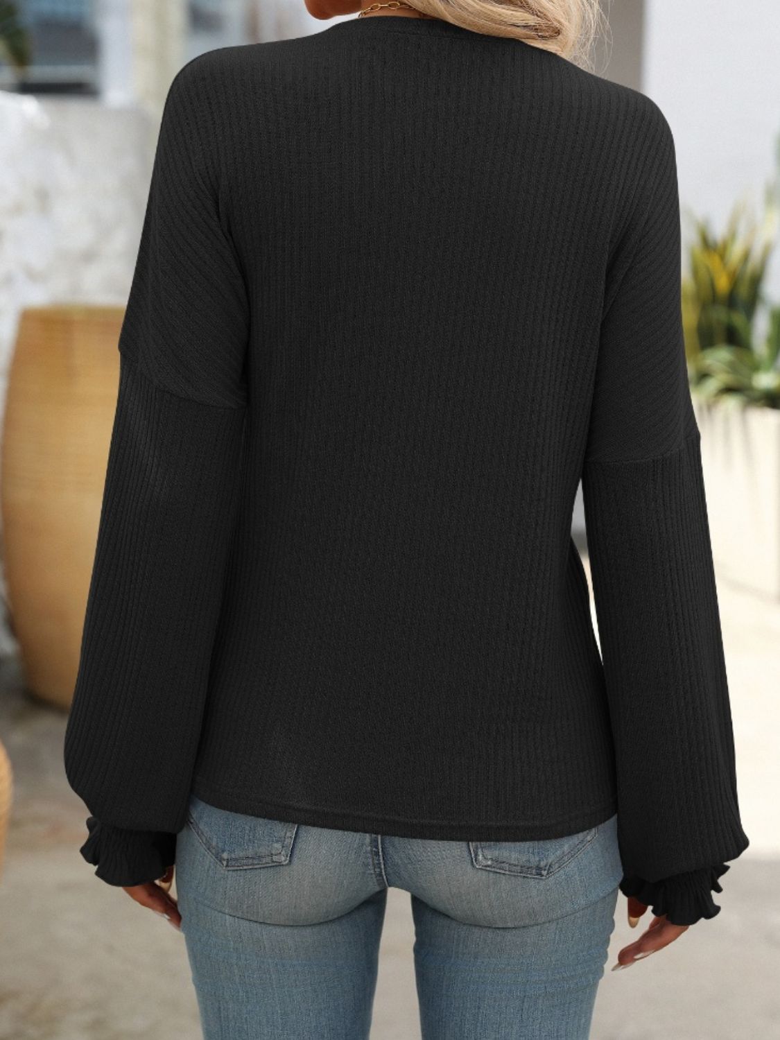 Black ribbed knit blouse with ruffled cuffs and long sleeves.