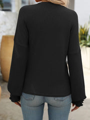 Black ribbed knit blouse with ruffled cuffs and long sleeves.